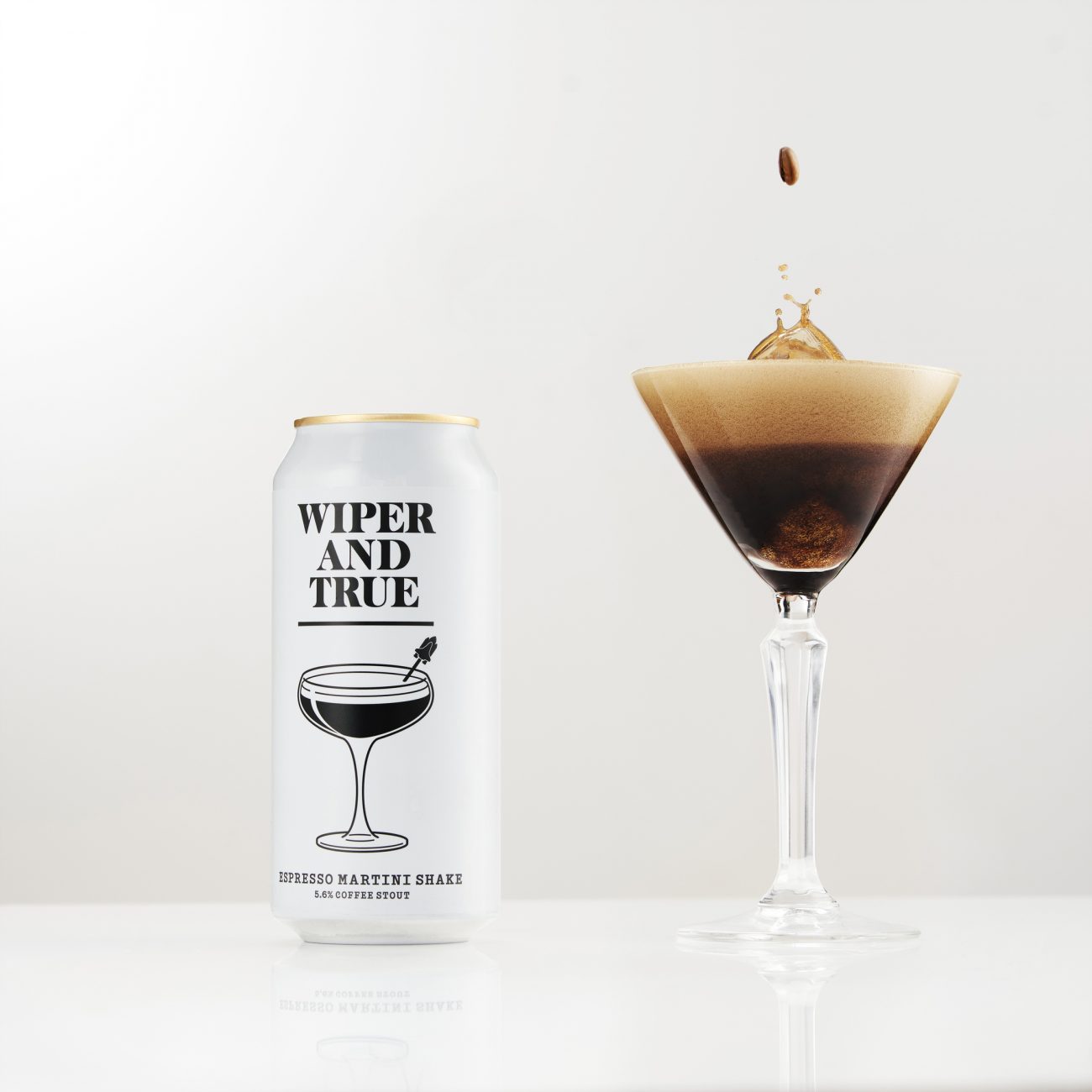 Studio photograph of a can of Wiper and True Espresso Martini Shake beer alongside a filled cocktail glass with a coffee bean splashing into the liquid