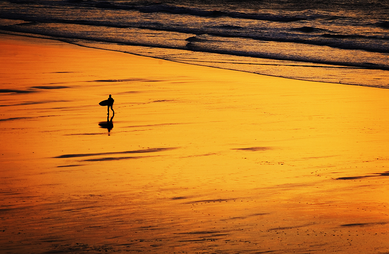 Surfer at sunset on Fistral Beach by Adam Gasson