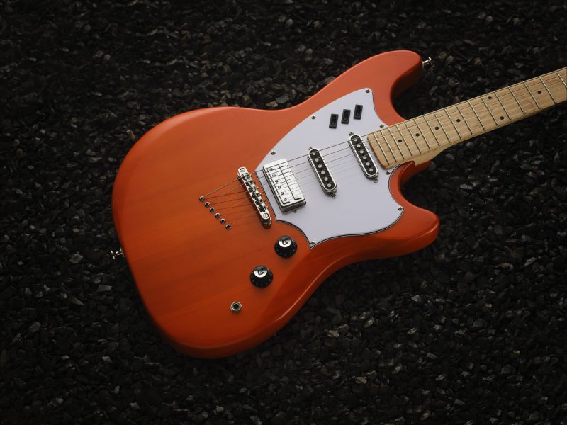 Studio photograph of a Guild Surfliner guitar in orange on dark rocks