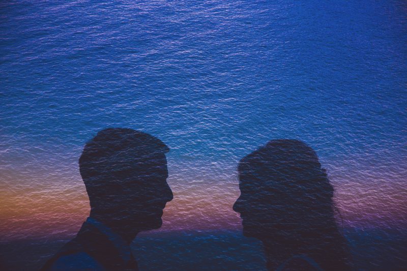 A couple on their wedding day with waves behind them at sunset