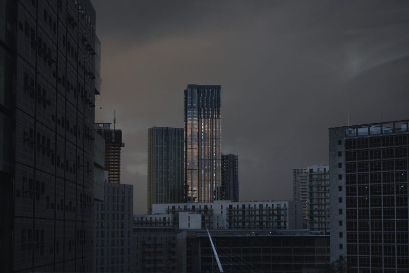 Manchester centre skyline at dusk with the setting sun reflecting off a glass office block in the centre of the image