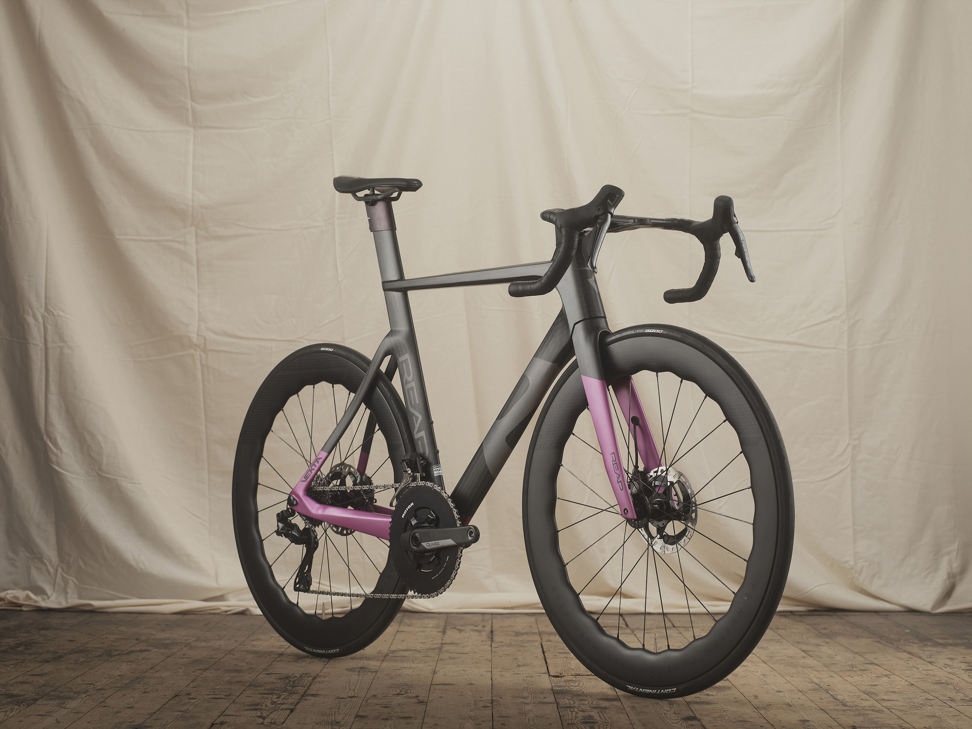 Photograph of a REAP cycles carbon fibre road bike against a fabric background and wooden floor