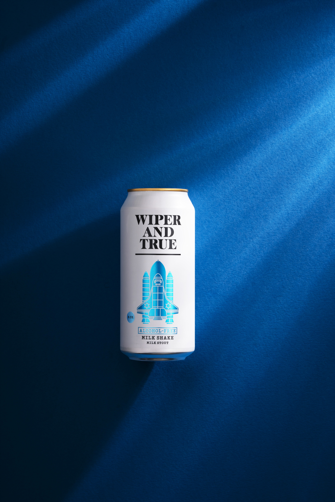 Studio photograph of a can of Wiper and True Alcohol Free Milk Shake taken from overhead on a dark blue background and shards of light coming from the top right of the frame