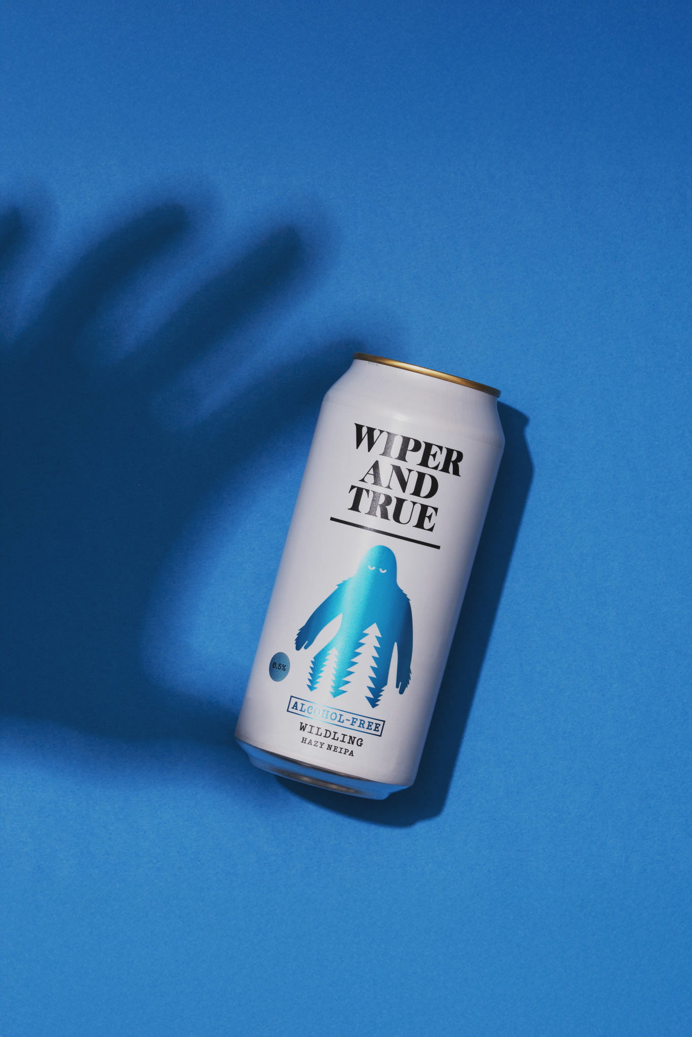 Studio photograph of a can of Wiper and True Wilding beer from overhead on a blue background. There is a shadow of a hand reaching for the can