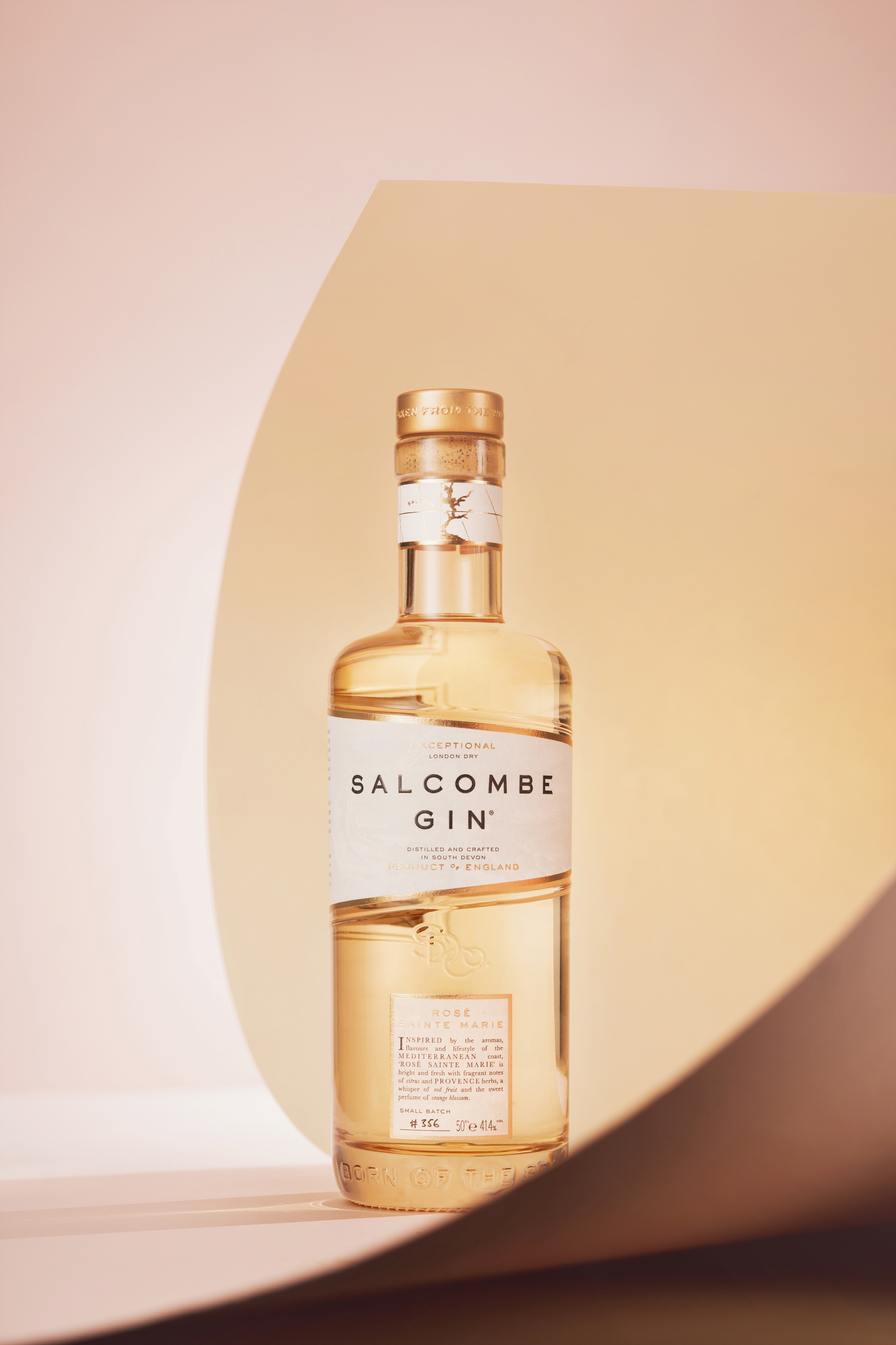 Studio photograph of a bottle of Salcombe Gin on a peach and pink background